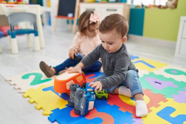 Sevimli çocuk ve kız arabalarla oynuyorlar. Anaokulunda yerde oturuyorlar.