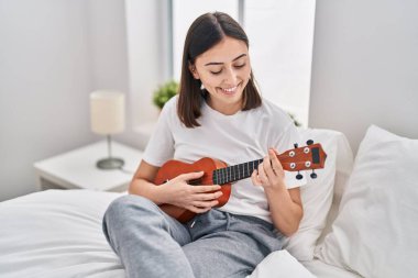 Genç İspanyol kadın yatakta ukelele oynuyor.