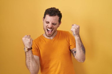 Young hispanic man standing over yellow background celebrating surprised and amazed for success with arms raised and eyes closed. winner concept. 