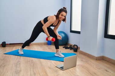 Genç, güzel, İspanyol bir kadın spor merkezinde online eğitim aldığından emin bir şekilde gülümsüyor.