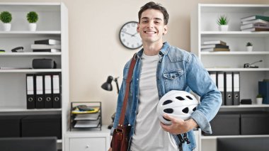 Ofiste bisiklet kaskı tutan genç İspanyol iş adamı gülümsüyor.