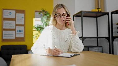 Genç sarışın iş kadını. Ofisteki panoda akıllı telefon yazısıyla konuşuyor.