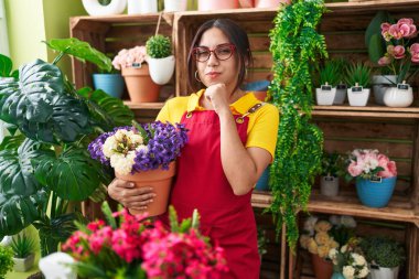 Çiçekçi dükkanında çalışan genç Arap kadın elinde bitkiyle ciddi bir yüz ifadesi olan eli çenesinde soruyu düşünen, kafa karıştırıcı fikirleri düşünceli bir kadın. 