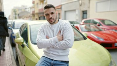 Sokakta kolları çaprazlanmış bir şekilde arabada oturan İspanyol genç adam.