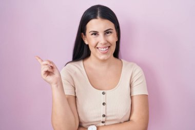 Pembe arka planda duran genç İspanyol kadın yüzünde büyük bir gülümsemeyle, kameraya el ile işaret ederek bakıyor.. 