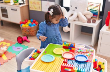 Adorable hispanic girl standing with relaxed expression at kindergarten