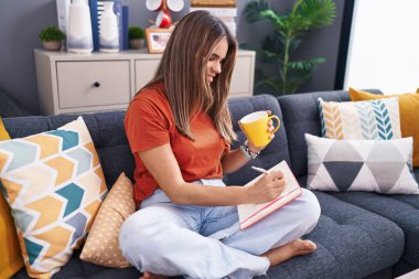 Genç, güzel İspanyol bir kadın deftere yazıyor. Evdeki kanepede oturup kahve içiyor.