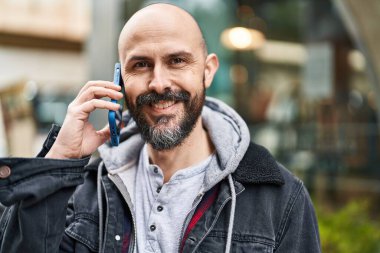 Genç kel adam gülümsüyor. Kendine güveni tam. Akıllı telefondan konuşuyor.