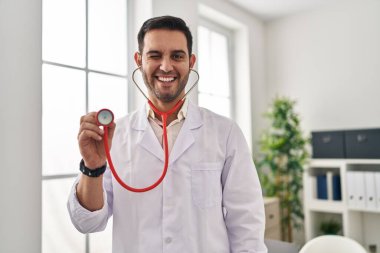 Sakallı, steteskop tutan genç İspanyol doktor kameraya seksi bir ifadeyle bakıyor, neşeli ve mutlu bir yüzle.. 