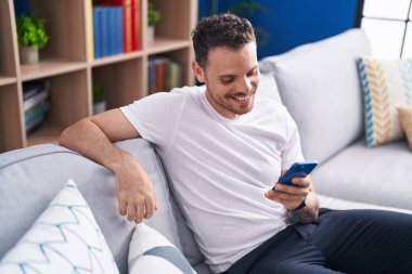 Evdeki kanepede oturan, akıllı telefon kullanan genç bir İspanyol.