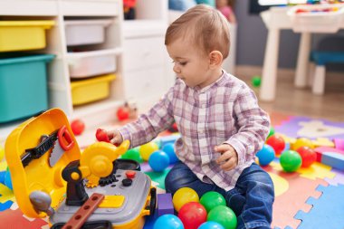 Anaokulunda yerde taşaklarıyla oynayan sevimli beyaz çocuk.