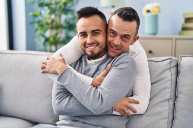 Two men couple hugging each other sitting on sofa at home