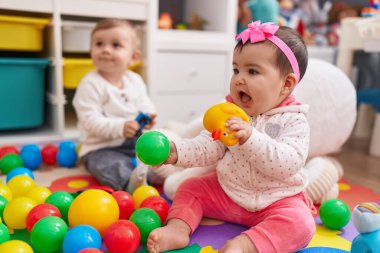 Anaokulunda yerde oturmuş toplarla oynayan sevimli bir kız ve erkek çocuk.