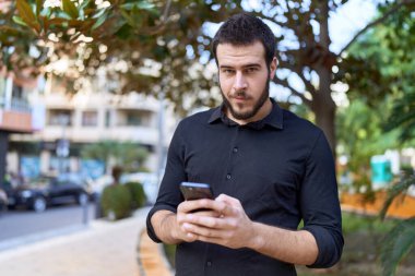 Parkta akıllı telefon kullanarak gülümseyen İspanyol genç adam.