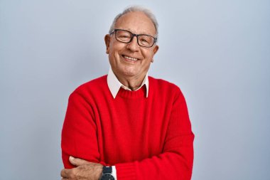 İzole edilmiş arka planda gri saçlı yaşlı adam kollarını kavuşturup kameraya bakarken gülümsüyor. pozitif kişi. 