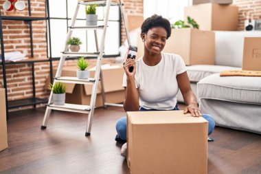 Afrika kökenli Amerikalı kadın, karton kutu paketliyor. Yeni evinde yerde oturuyor.