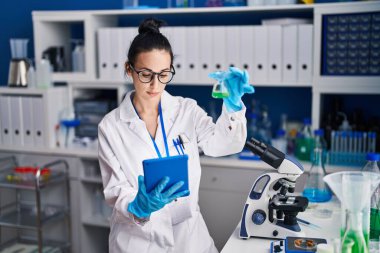 Genç beyaz kadın bilim adamı laboratuarda dokunmatik ped kullanarak test tüpü tutuyor.