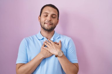 Pembe arka planda duran İspanyol adam elleri göğsünde, gözleri kapalı ve yüzünde minnet dolu bir jest ile gülümsüyor. sağlık kavramı. 