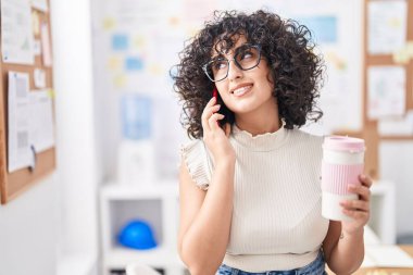 Ortadoğulu genç iş kadını akıllı telefondan konuşuyor ofiste kahve içiyor.