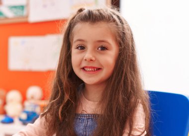 Adorable hispanic girl smiling confident sitting on table at kindergarten