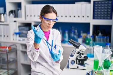 Young beautiful hispanic woman scientist pouring liquid on sample at laboratory