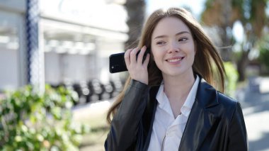 Genç sarışın kadın gülümsüyor. Parktaki akıllı telefondan kendine güvenen sesli mesaj dinliyor.