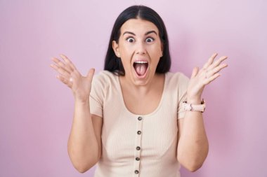 Pembe arka planda duran genç İspanyol kadın çılgın ve başarıyı kollarını kaldırıp heyecanla haykırarak kutluyor. Kazanan konsept 