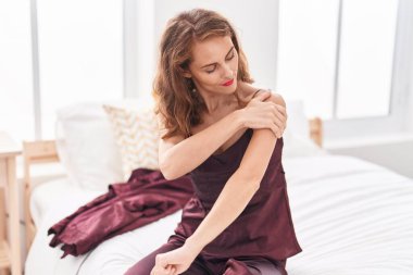 Genç ve güzel İspanyol kadın omuz ağrısı çekiyor. Yatak odasında oturuyor.