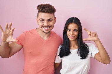 Pembe arka planda duran genç İspanyol çift gülümsüyor ve el hareketleriyle el hareketleriyle küçük boy işareti yapıyor ve kameraya bakıyor. ölçüm kavramı. 