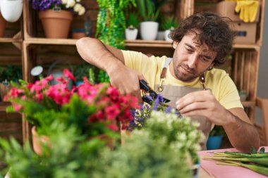 Young hispanic man florist cutting plant at flower shop