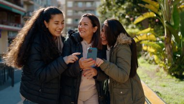 Mother and daugthers using smartphone standing together at park