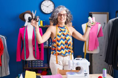 Orta yaşlı, gri saçlı, sırıtan bir kadın. Elinde makas ve dikiş atölyesinde iplik tutan kendine güvenen bir terzi.