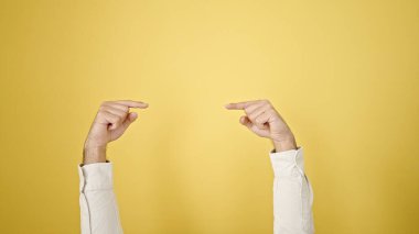 Genç İspanyol adam izole edilmiş sarı arka planda boş bir alanı işaret ediyor.