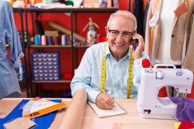 Orta yaşlı, kır saçlı bir terzi atölyedeki defterde akıllı telefon yazısıyla konuşuyor.