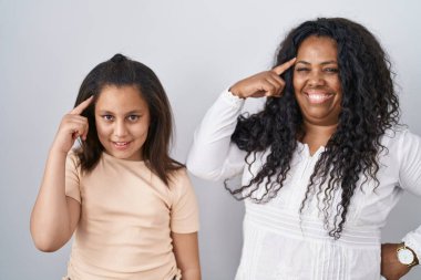 Anne ve küçük kızı beyaz arka planda durup gülümsüyor ve tek parmağıyla kafasını işaret ediyor. Harika bir fikir ya da düşünce, iyi bir hafıza. 