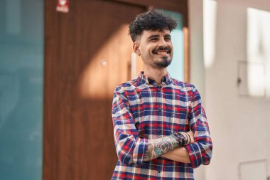 Young hispanic man smiling confident standing with arms crossed gesture at street