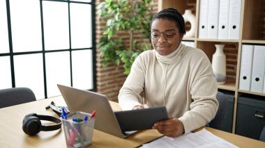 Ofiste dokunmatik ped ve laptop kullanan Afrikalı Amerikalı iş kadını.