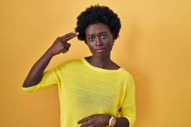 Afrikalı genç bir kadın sarı stüdyonun başında durup kendini silahla ve parmaklarla işaret ederek vuruyor, intihar ediyor.. 