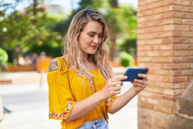 Sokakta akıllı telefondan video seyreden kendine güvenen genç bir kadın.