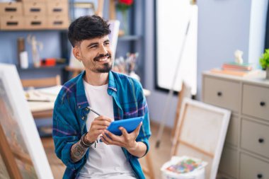 Young hispanic man artist smiling confident drawing on touchpad at art studio