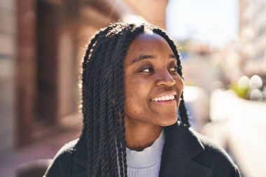 Afro-Amerikalı kadın gülümsüyor. Kendinden emin bir şekilde caddeye bakıyor.