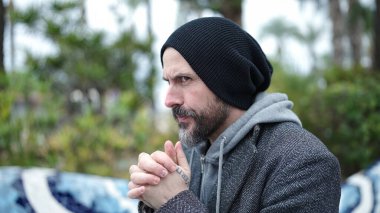 Genç kel adam parkta dua ediyor.