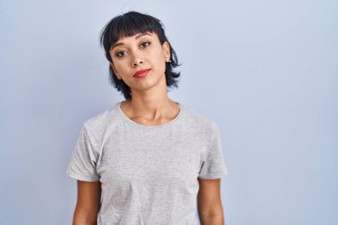 Mavi arka plan üzerine gündelik tişört giyen genç İspanyol kadın yüzünde ciddi bir ifadeyle rahatladı. Basit ve doğal bir şekilde kameraya bakıyorsun.. 