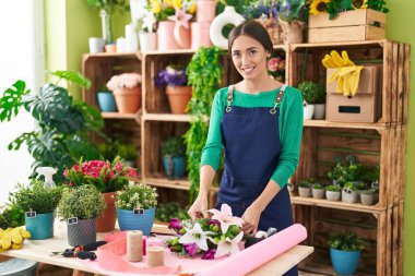 Young beautiful hispanic woman florist make bouquet of flowers at flower shop