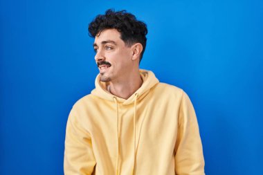 Mavi arka planda duran İspanyol bir adam yüzünde gülümseme, doğal bir ifade ile yan yana bakıyor. Kendinden emin gülen. 