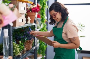 Young woman florist smiling confident writing on clipboard at florist