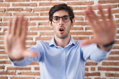 Tuğla duvar arkasında duran genç İspanyol adam avuç içi hareketlerini durduruyor, kızgın ve hayal kırıklığına uğramış yüz ifadesi. 