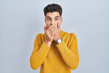 Mavi arka planda dikilen İspanyol genç adam yanlışlıkla ağızlarını kapatarak şok geçirdi. gizli kavram. 