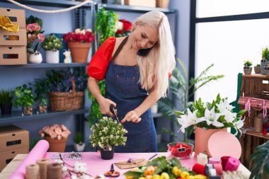 Çiçekçide çiçekçiyle konuşan sarışın bir kadın.