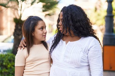 Anne ve kızı parkta birbirlerine ciddi bir şekilde sarılıyorlar.